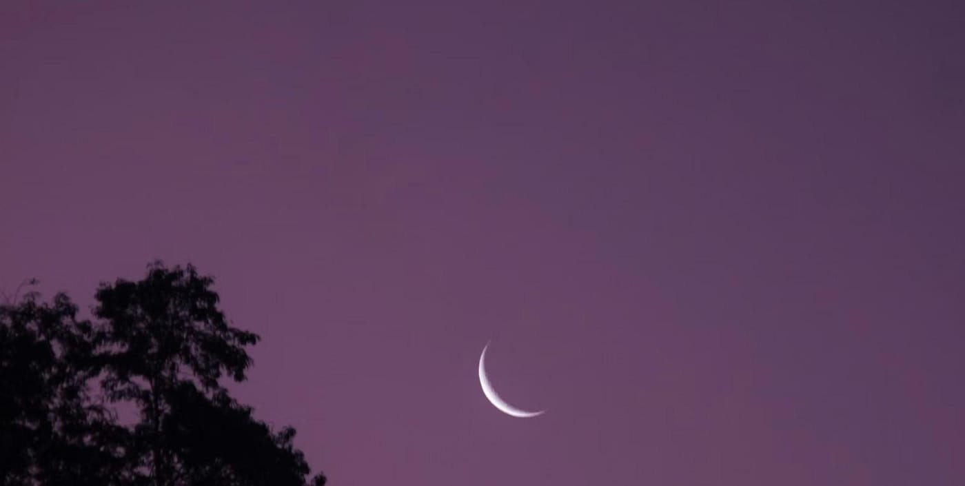 A thin crescent moon in a purple twilight sky